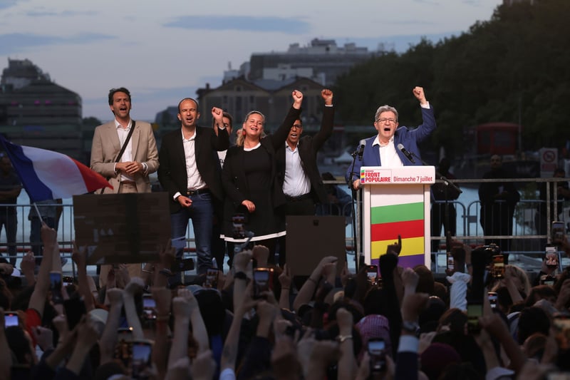 Politicians raise their fists on an outdoor stage above a crowd.