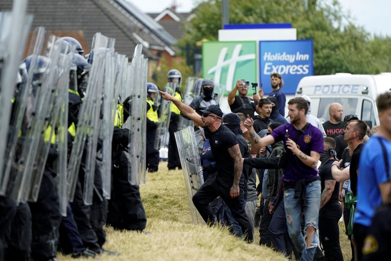A line of protesters faces off against a line of police officers with shields.
