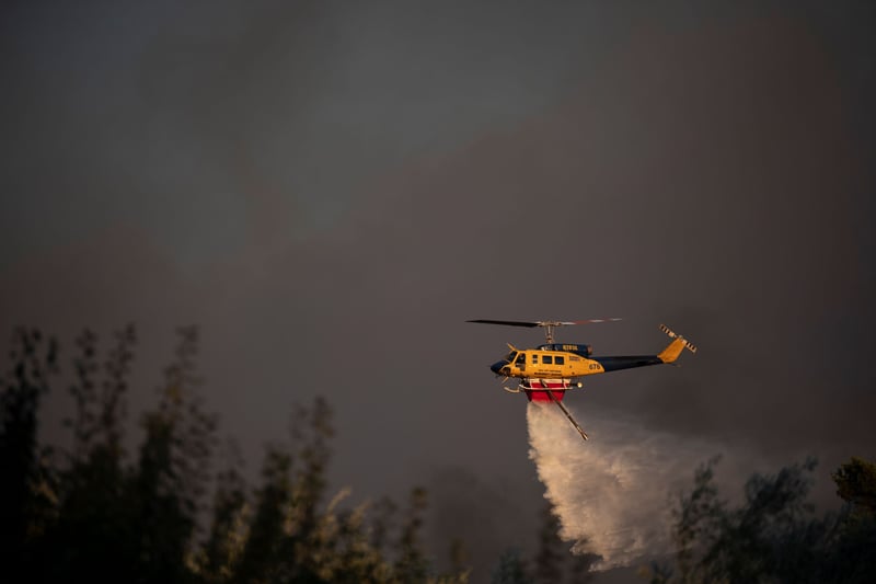 A helicopter dumps water on trees against a smoky backdrop.
