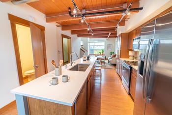 Modern kitchen with large island, stainless steel appliances, wood beam ceilings, and open view into the living room.