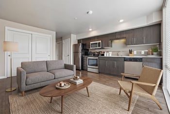 Open concept living room and kitchen with dark modern cabinets, stainless appliances, grey sofa, and coffee table.