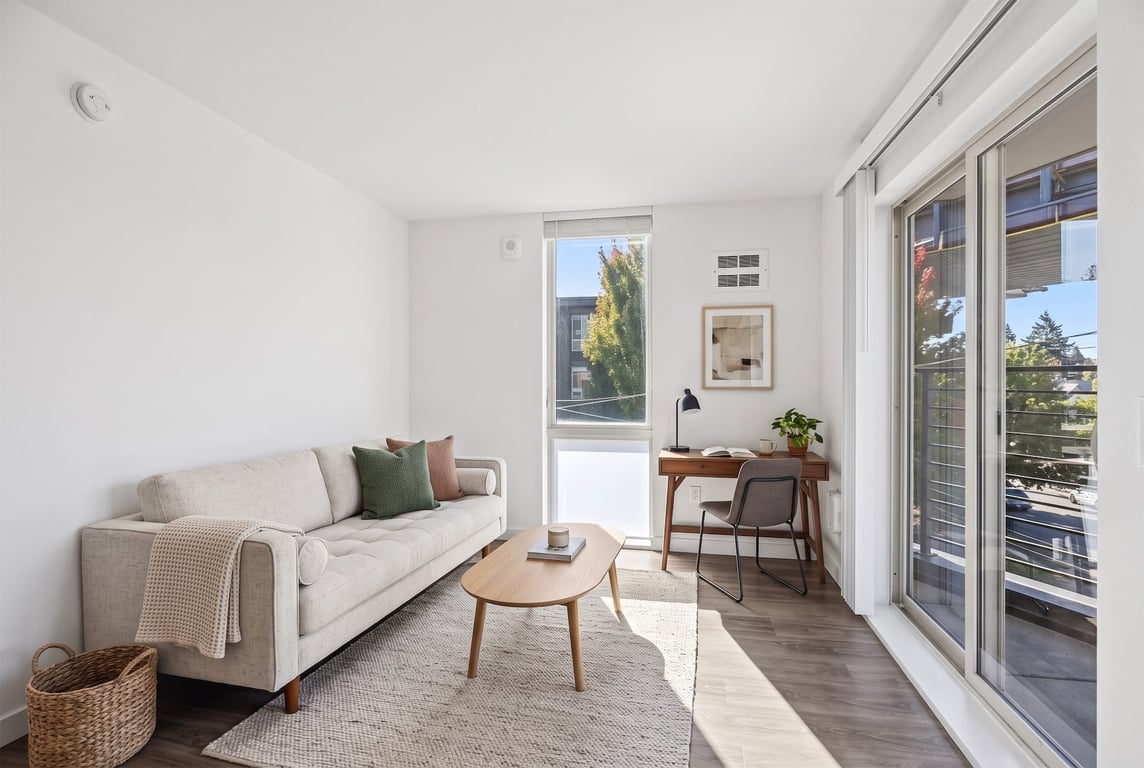 Spacious living room with light sofa, wooden desk, coffee table, and sliding glass door to a priv...