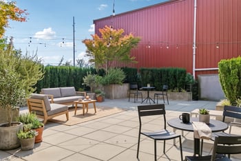 Outdoor resident patio at REV Fremont with lounge seating, bistro tables, potted plants, and string lights.