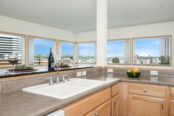 A kitchen with a sink, a bowl of fruit, and a view of the city.