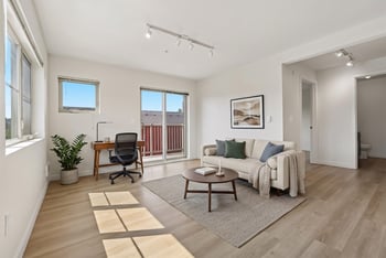 Bright living room with wood-style floors, sofa, coffee table, desk, and sliding door to balcony.