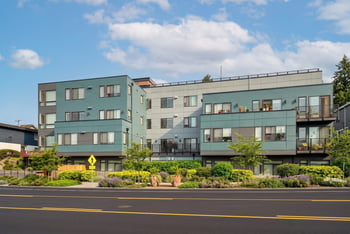 Lanterman Apartments seen from the street with a yellow pedestrian crossing sign and landscaped sidewalk.