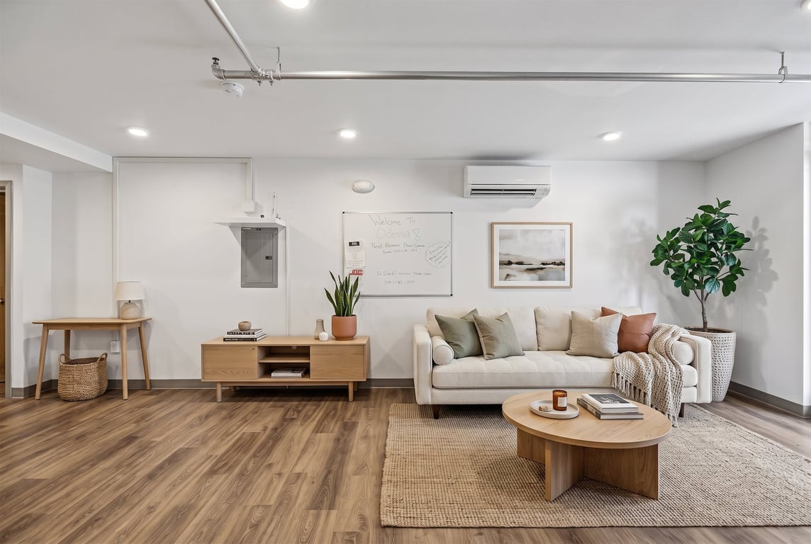 Community lounge at Odessa Apartments with a light sofa, wood floors, a desk, and a whiteboard.