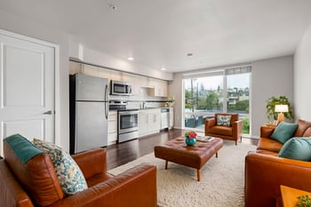 Spacious open-concept living room and kitchen with brown leather furniture and stainless steel ap...