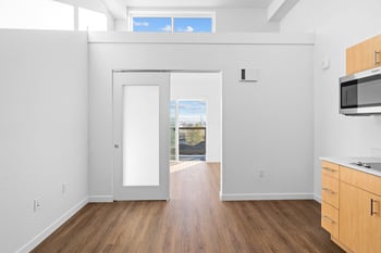 a kitchen with white walls and wooden floors and a door to a balcony