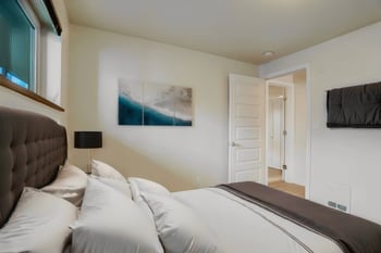 Bedroom with a bed, window, and door to another room, viewed from a different angle.