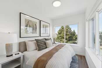 Bright bedroom with a comfortable bed, nightstands, decorative art, and large windows looking out...