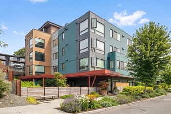 Corner view of Lanterman Apartments with wood and teal siding, private balconies, and landscaped beds along the sidewalk.