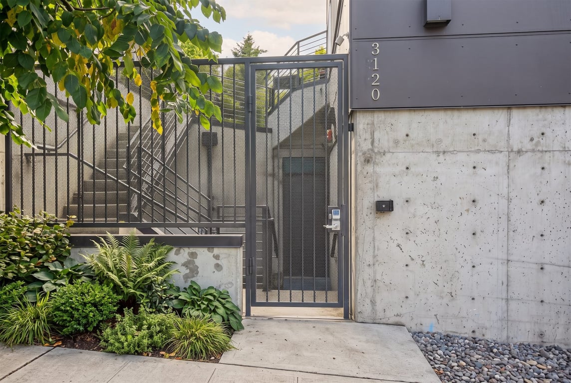 Building exterior entrance with metal security gate, concrete wall, address 3120, and green lands...