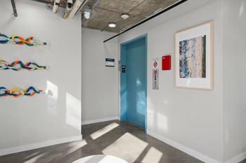 Modern hallway with bright blue elevator, concrete floor, exposed ceiling, colorful wall art, and...