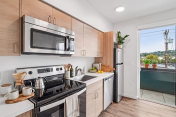 Kitchen with wood-tone cabinets and stainless steel appliances beside a sliding glass door to a private balcony.