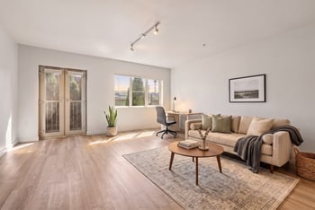 Living area with beige sofa, coffee table, desk workspace, and French doors leading outdoors.