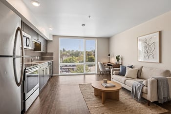 Open-concept kitchen and living room with stainless steel appliances, wood floors, a sofa, and a ...