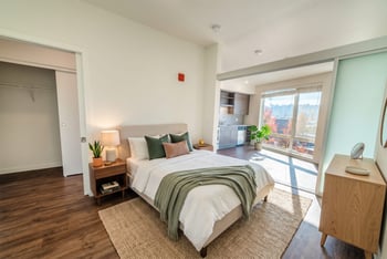 Staged bedroom area with closet access, sliding partition door, and open view into the kitchen.