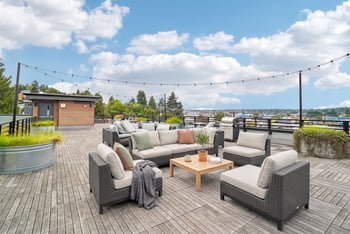 Rooftop deck lounge with sectional sofas, cushioned armchairs, a wood coffee table, and string lights.