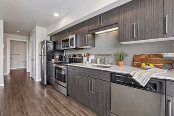 Modern kitchen with dark wood-grain cabinets, stainless steel appliances, tile backsplash, and wood-style flooring.