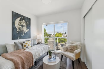 Bedroom with a bed, large window overlooking a street, an armchair, and a sliding closet door.