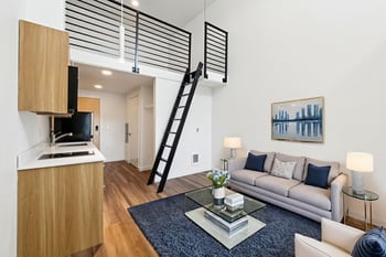 A living room with a grey couch and a black ladder.