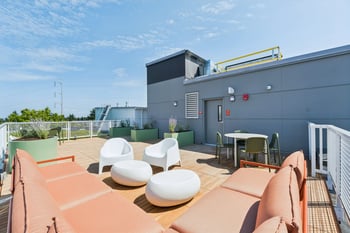Rooftop patio with coral lounge, white chairs, round tables, and a dining set on wood deck.