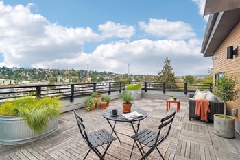 Rooftop deck with a bistro table and chairs, lounge seating, and planters overlooking the neighborhood.