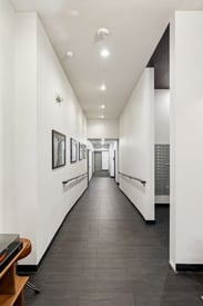 Well-lit apartment building hallway with dark tiled floor, white walls, handrails, framed art, an...