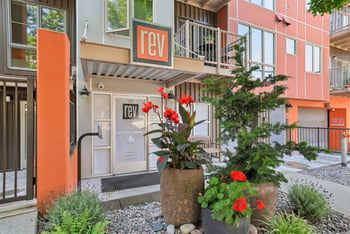 REV Fremont building entrance with orange signage, modern siding, and potted plants in the foreground.