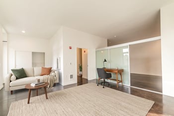 Living area with modern sofa, desk, concrete flooring, and sliding glass partition.
