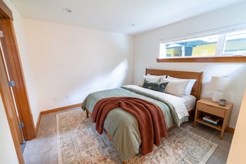 Staged bedroom at Union Bay Lofts with a wooden bed, nightstand, neutral carpet, and high horizontal window.