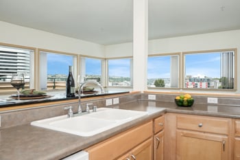 A kitchen with a sink, a bowl of fruit, and a view of the city.