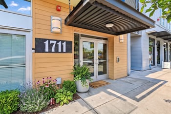 Street-level entrance of Ludwig Apartments at 1711 with glass double doors, modern awning, and potted plants.