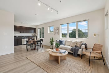 Open living room with couch, dining table, and dark kitchen cabinetry under large windows at REV Fremont.
