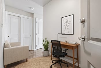 Work nook with wooden desk, mesh chair, armchair, and sliding closet doors at Ludwig Apartments.