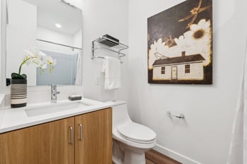 Modern bathroom with light wood vanity, white countertop, rectangular sink, mirror, toilet, and s...