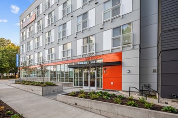 Modern gray and white apartment building exterior with orange accent entrance, balconies, and str...
