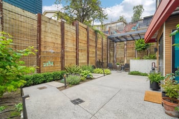 Landscaped garden courtyard with a cedar fence, ferns and ornamental grasses, path lighting, and patio seating.