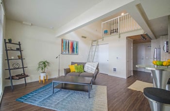 Bright Seattle Larson Building apartment living room with large windows, neutral decor, and modern kitchen for rent.
