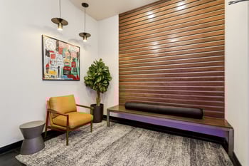 Modern common area with a wooden slatted accent wall, leather armchair, bench, abstract art, and ...