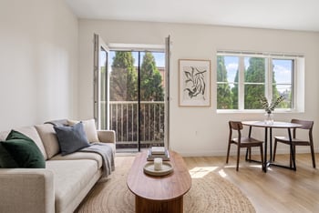 Staged living room with light sofa, wood coffee table, dining set, and open door to a balcony.