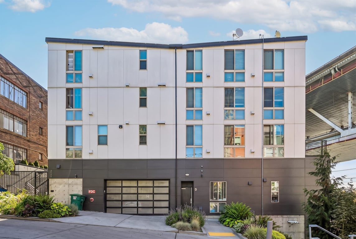 Modern apartment building exterior with white and gray panels, a garage, and landscaped entry.