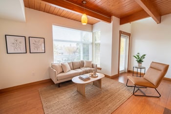 Living room with wood-paneled ceiling, beige sofa, coffee table, leather lounge chair, and large windows.