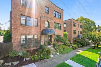 Brick exterior of East Highland Apartments building with a black entrance canopy and lush green l...