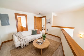 Upper-level loft sitting area with white sofa, round coffee table, and carpeted floor overlooking open railing.