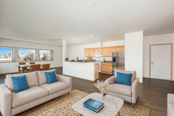 A living room with a couch, a coffee table, and a kitchen in the background.