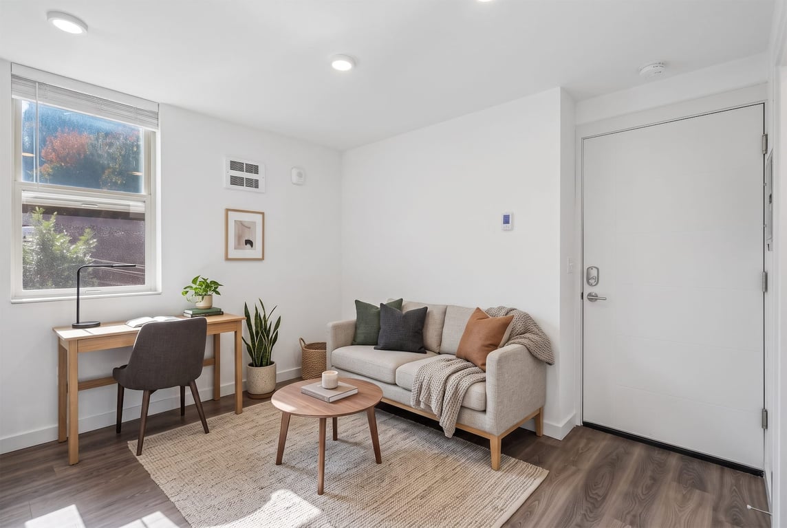 Living room at Odessa Apartments with a light gray sofa, wooden desk by a window, and coffee table.