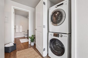 Stacked white washer and dryer in an open closet next to a bathroom doorway.