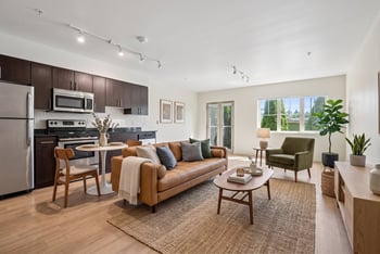 Open living room and kitchen with wood floors, leather couch, dining table, dark cabinets, and stainless appliances.